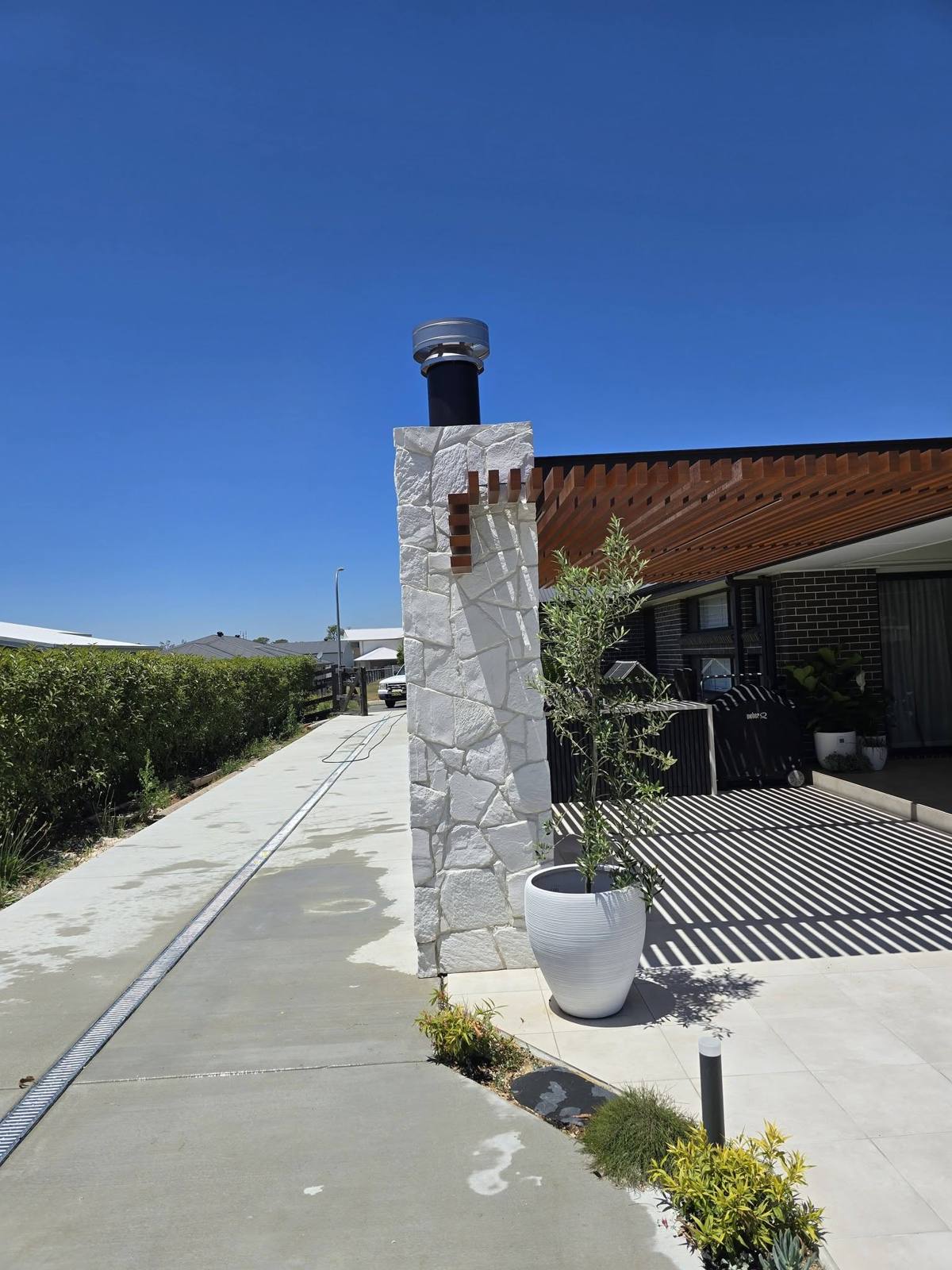 White stone-clad chimney feature beside a concrete driveway