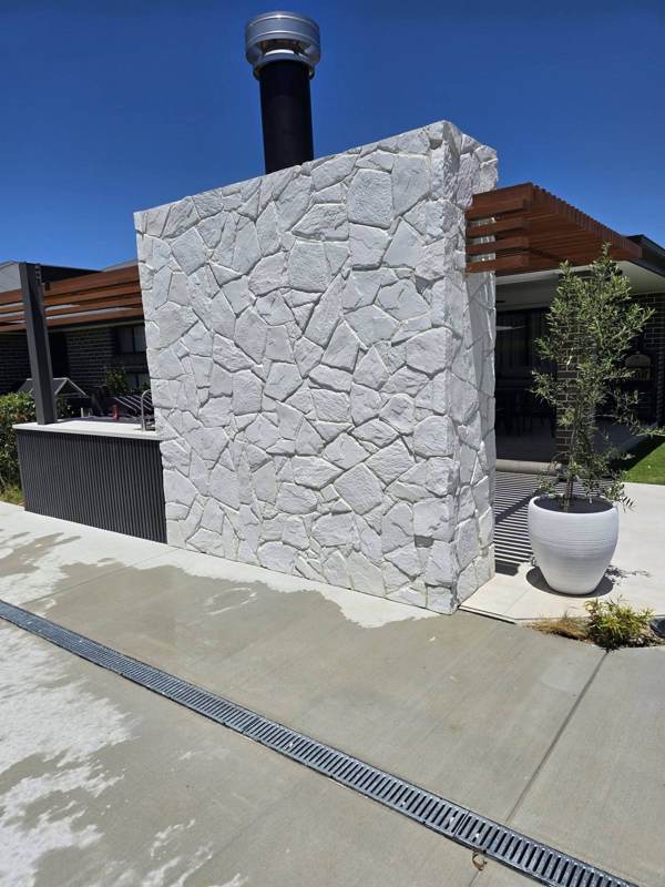 Concrete driveway with drainage channel beside a stone-clad feature wall